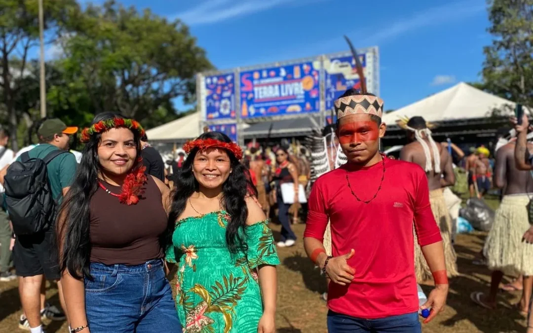 Imagem colorida mostra três jovens indígenas do Amazonas no Acampamento Terra Livre 2026
